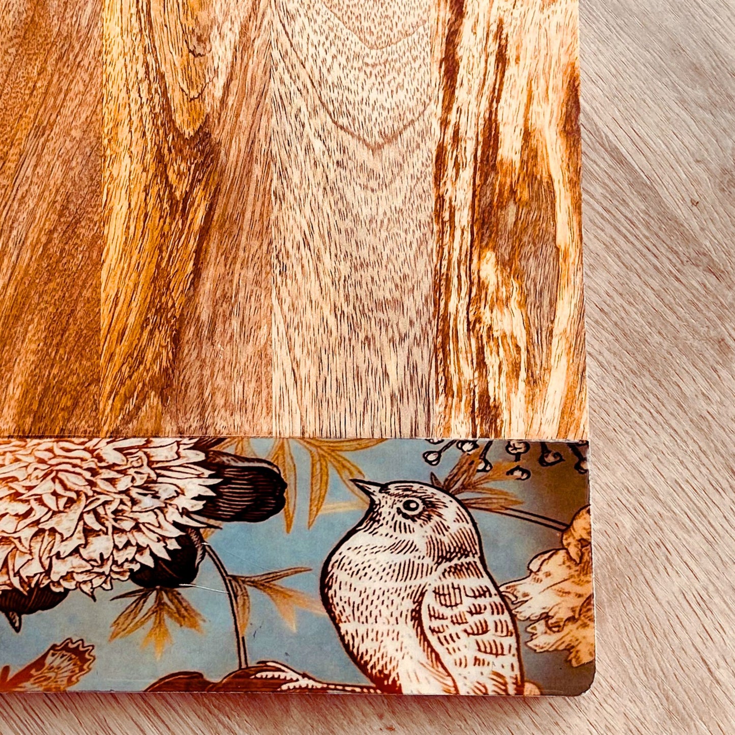 Close up of Mango Wood Cheese Board with handle. The Charcuterie Board has a nature, bird and flowers print at the bottom of the board.