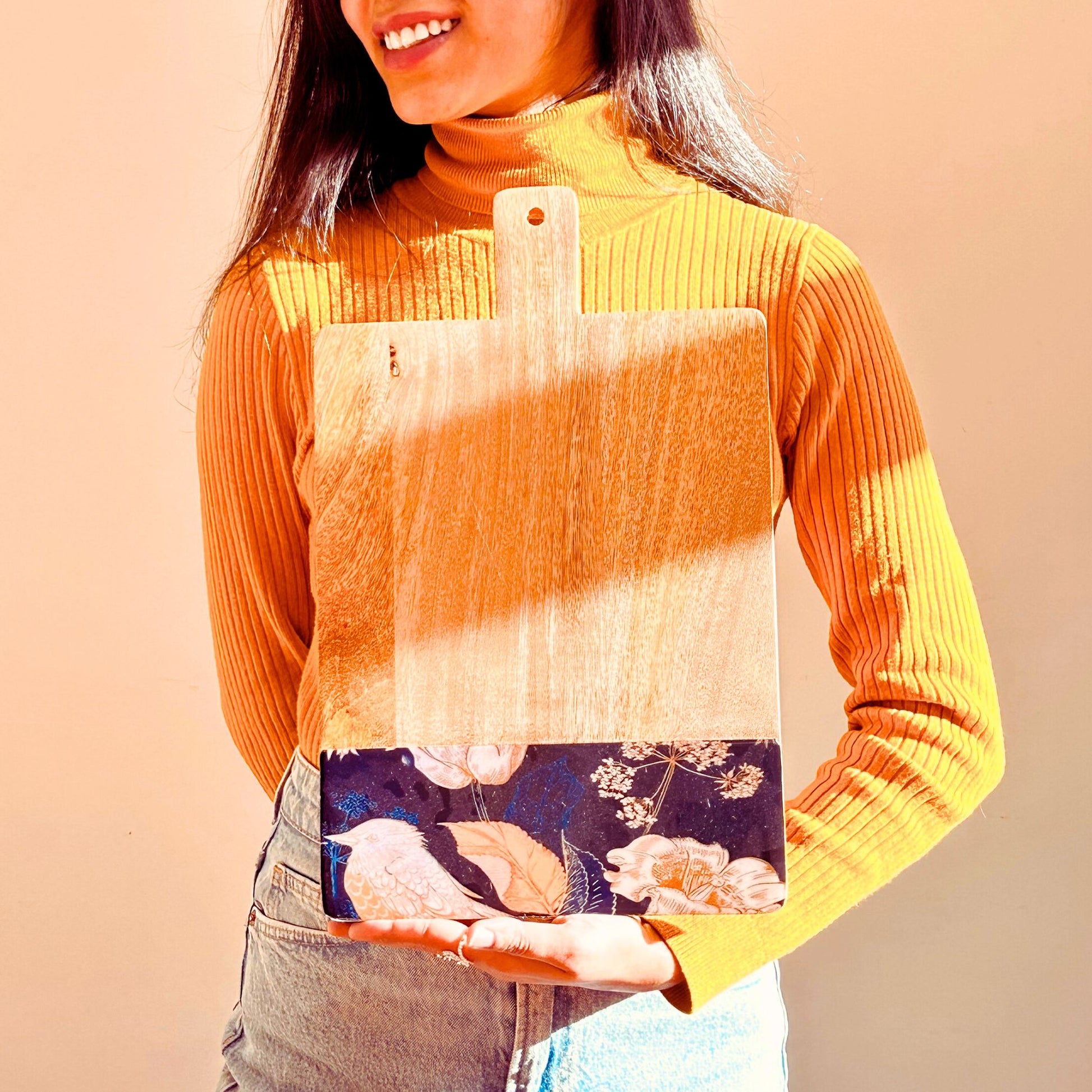 Model Holding a Mango Wood Cheese or Charcuterie Board with a print of bird, flowers and leaves on the bottom as a border