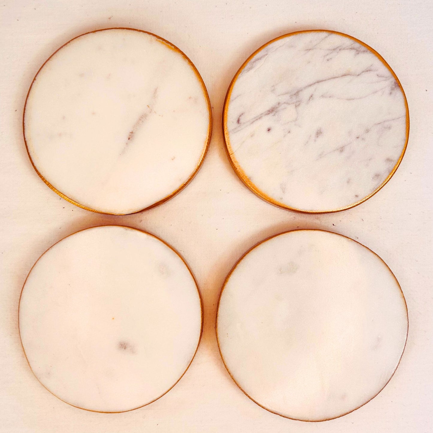 A set of 4 White round marble coasters with gold rim on a white background.