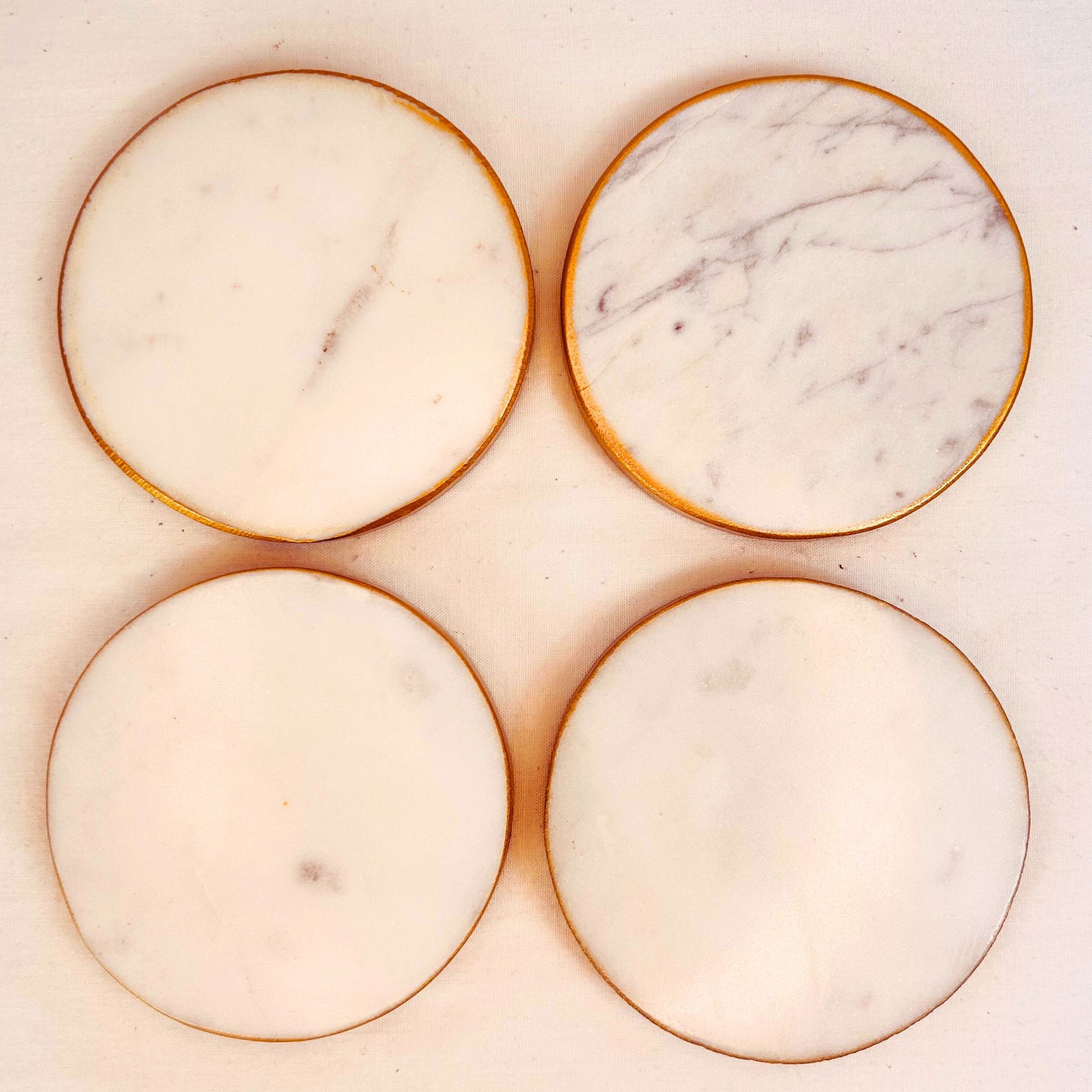 A set of 4 White round marble coasters with gold rim on a white background.