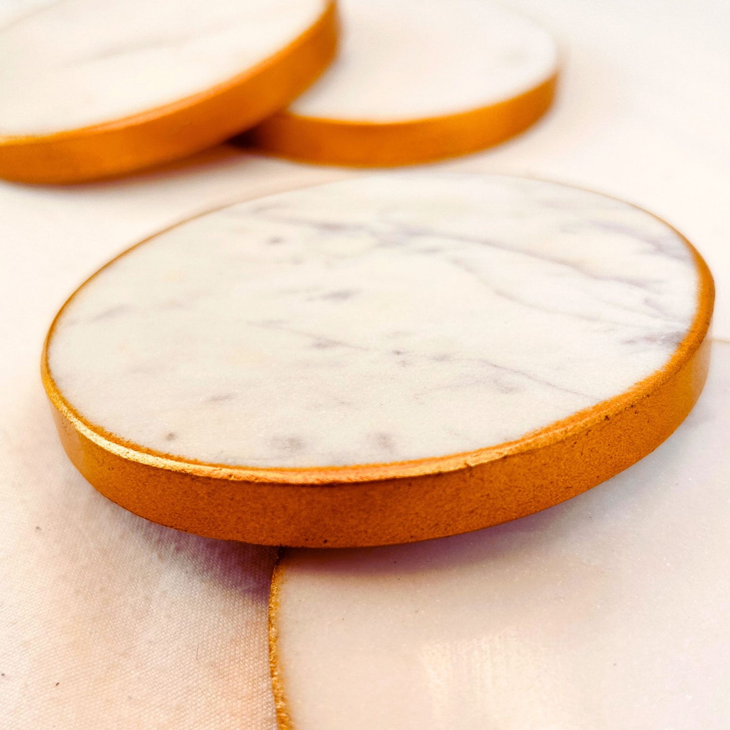 Close up of white round marble coasters with gold rim on a white background.