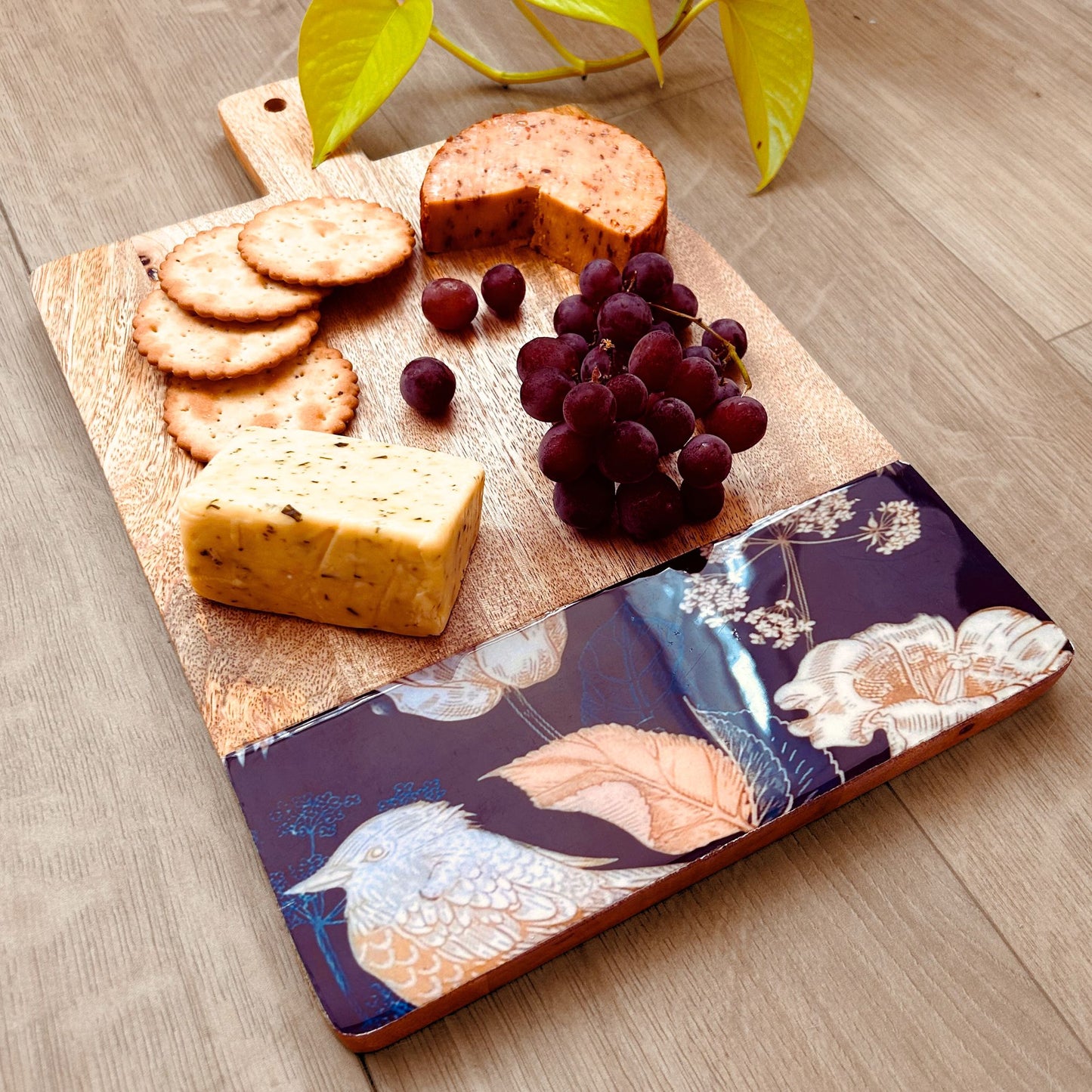 A spread of cheese, crackers and grapes on a Mango Wood Cheese or Charcuterie Board with print of bird, flowers and leaves on the bottom as a border