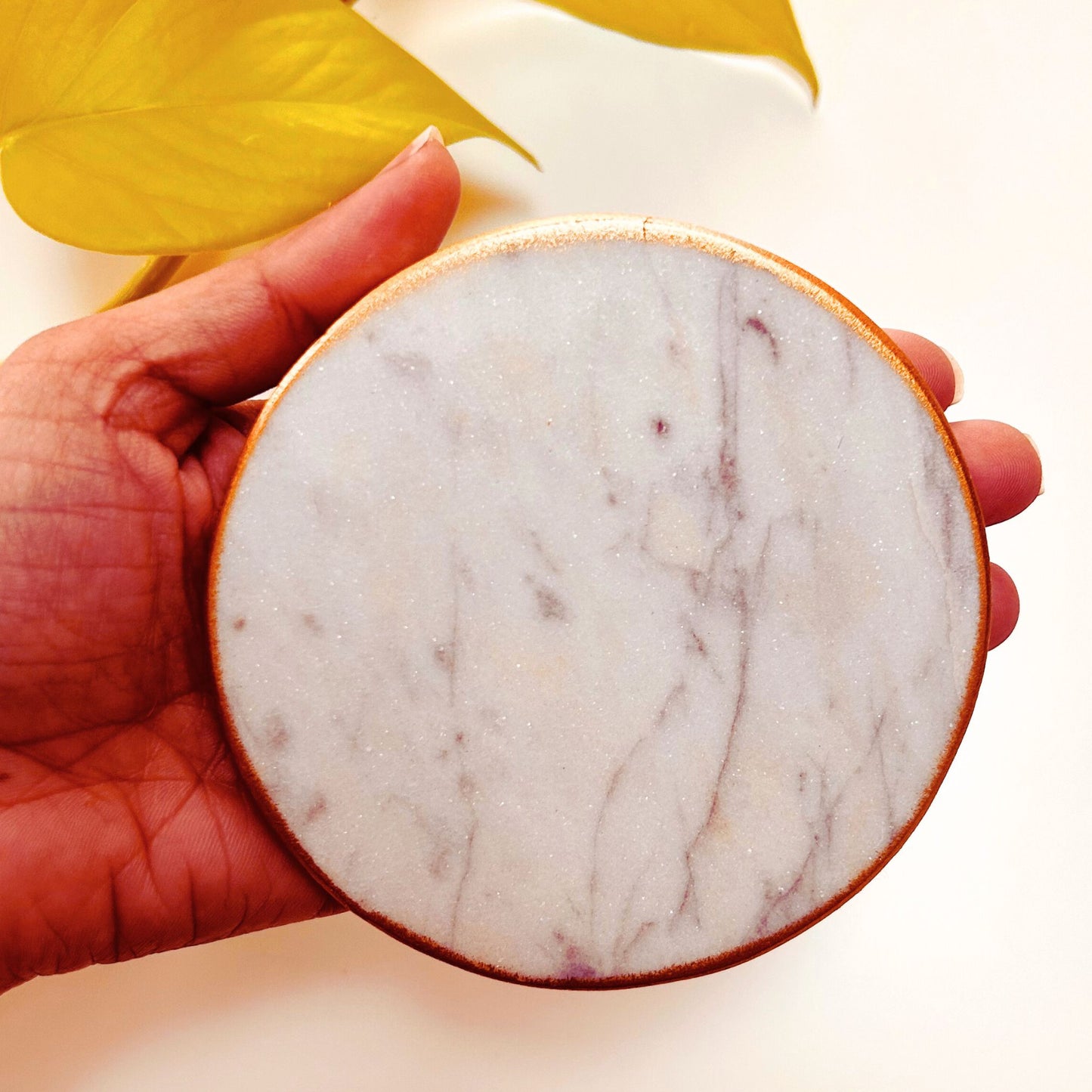 Hand holding a White round marble coasters with gold rim.