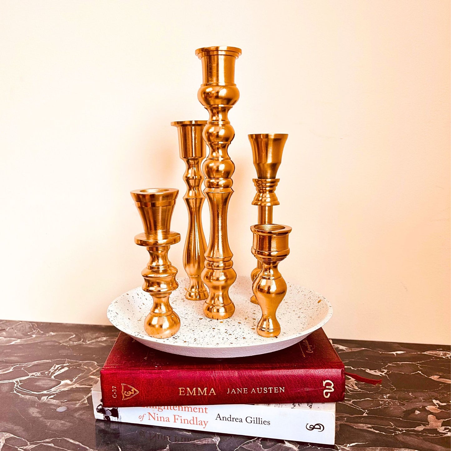 A 5 candle holder candelabra with a brass finish. The base is white with specks of gold on it.