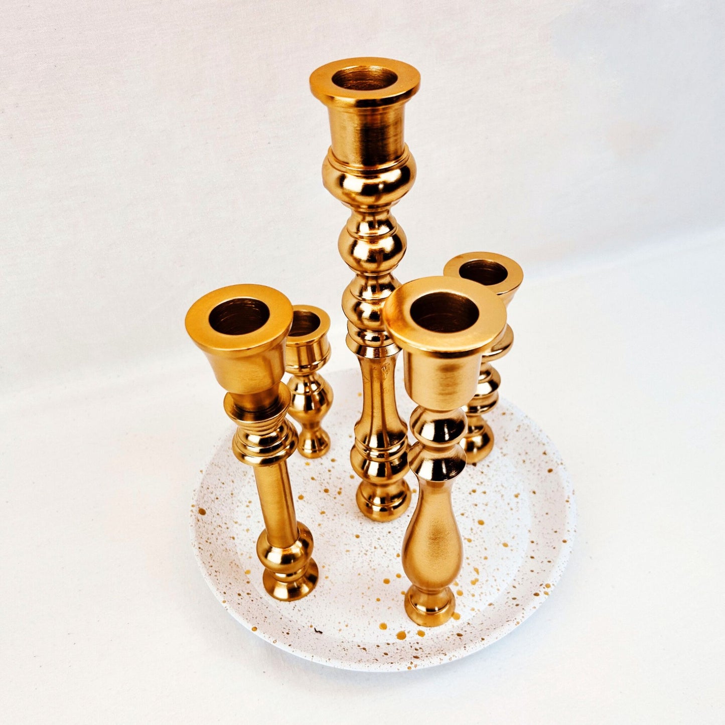 A 5 candle holder candelabra with a brass finish. The base is white with specks of gold on it.