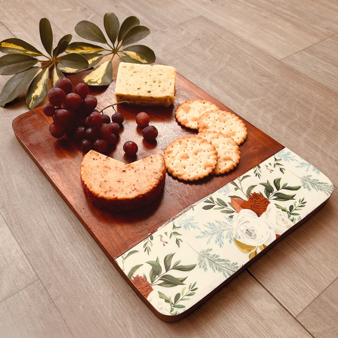 A spread of cheese, crackers and grapes on a Mango Wood Cheese or Charcuterie Board  with print of white roses, pinecones and leaves on the bottom as a border