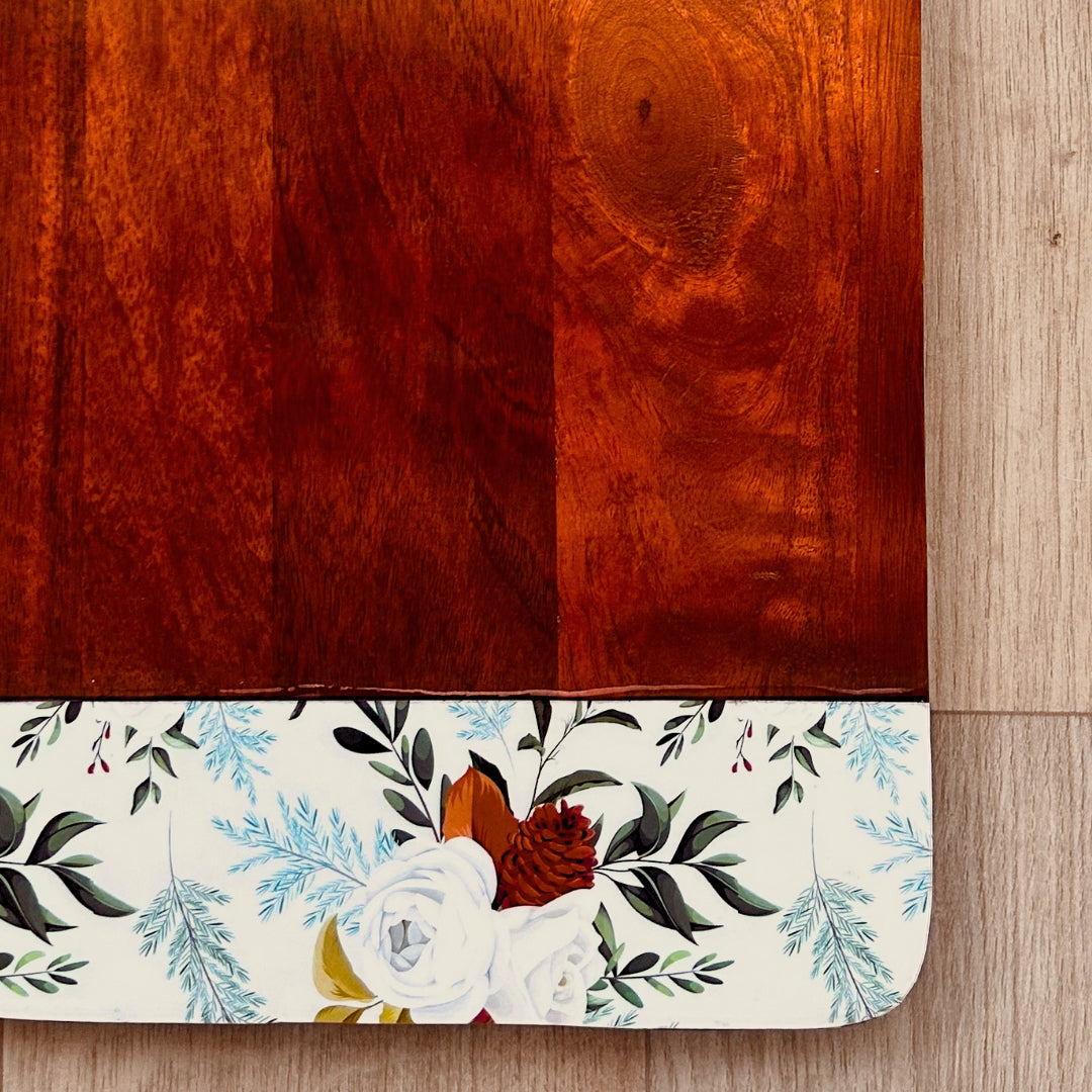 Close up of Mango Wood Cheese or Charcuterie Board  with print of white roses, pinecones and leaves on the bottom as a border