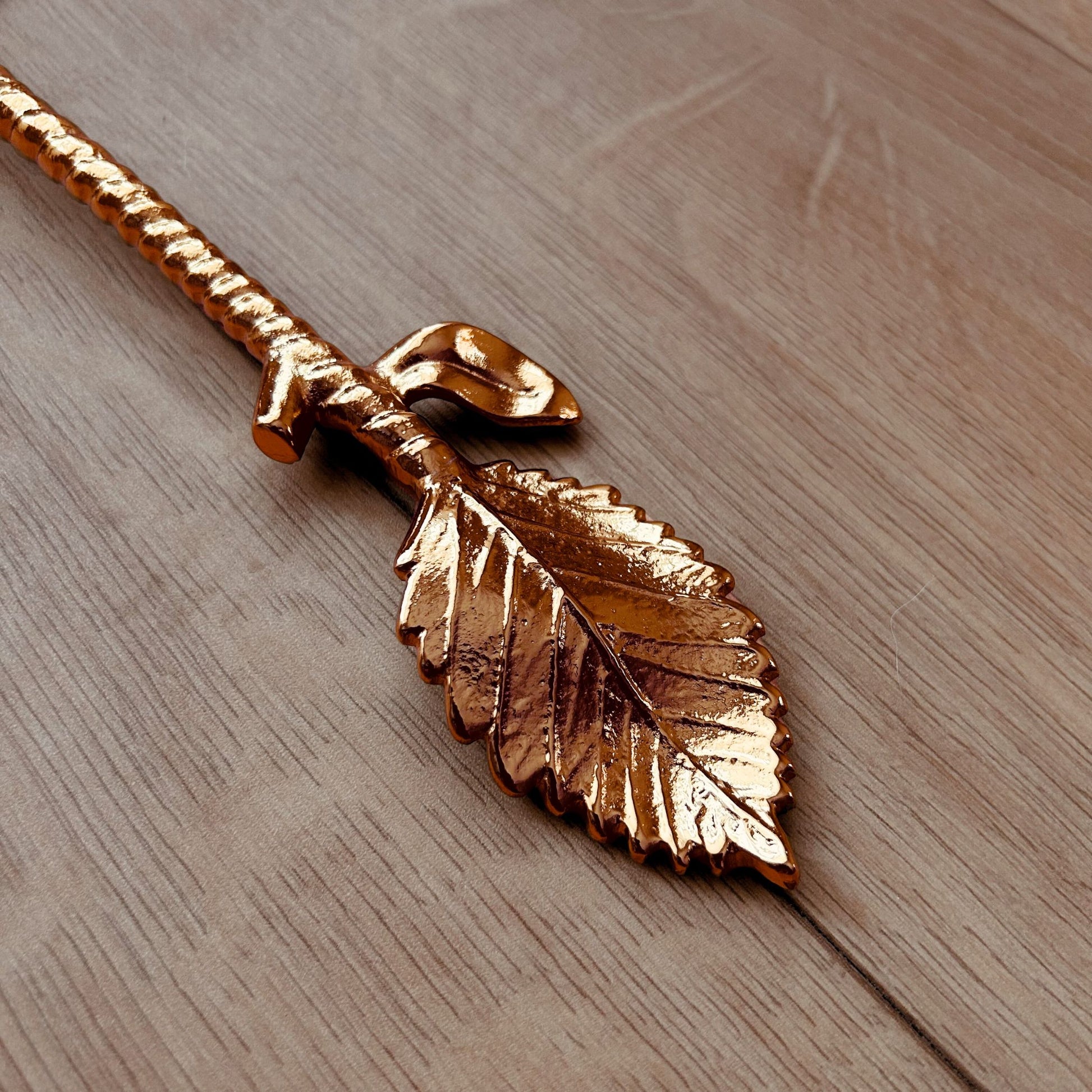 Close Up of a Gold Finish Stainless Steel Salad Serving Fork with a twine and leaf handle. It is kept on a wooden backdrop.