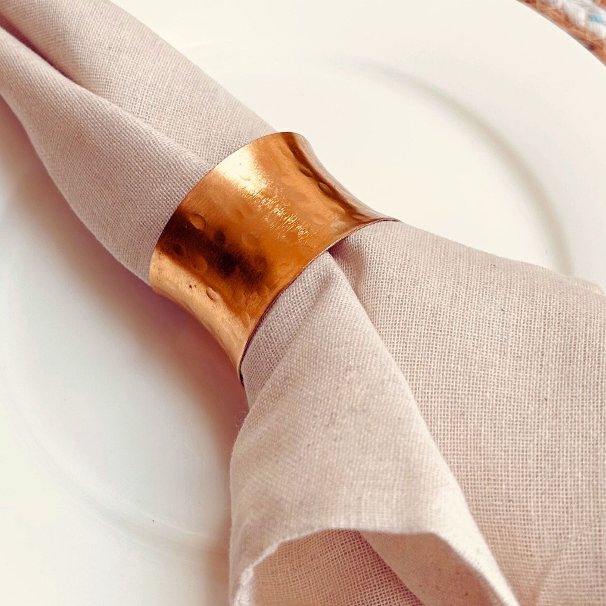 Gold Hammered Finish Napkin Ring. The napkin holder is on a white napkin which is kept on a white plate.