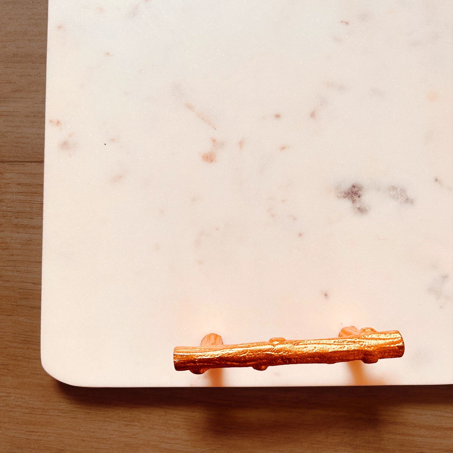 Close Up of a Rectangular White Marble Tray with Metal handles in gold finish kept on a wooden surface.