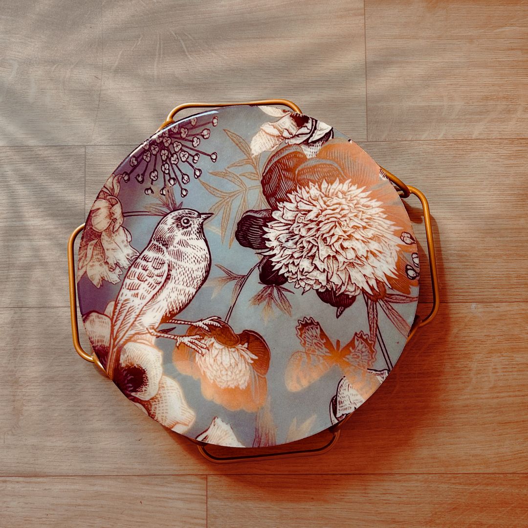 Cake Stand with Bird and flower print on a blue backdrop. The stand has an interlinked chain design in brushed gold.