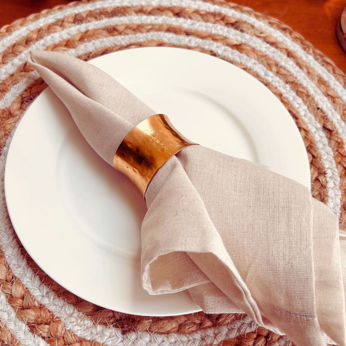 Gold Hammered Finish Napkin Ring. The napkin holder is on a white napkin which is kept on a white plate and a jute placemat.