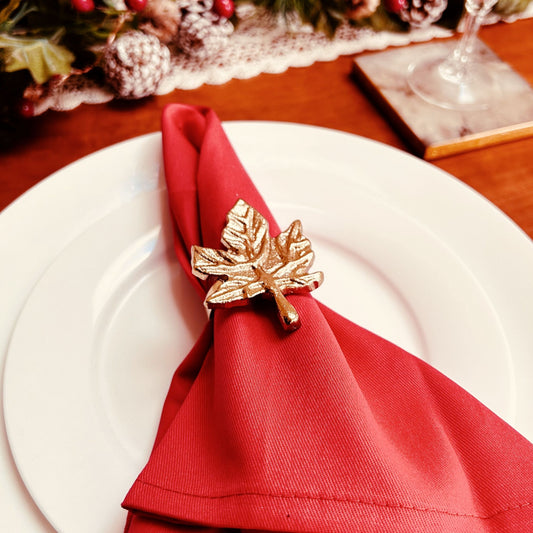 Gold finish Leaf design Napkin Ring placed on a red napkin ring kept on a white plate.