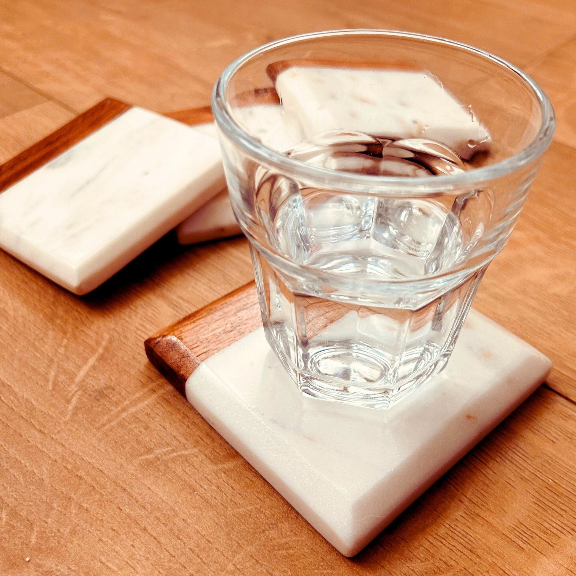 A set of 4 Acacia and Marble Drink Coasters with a drinking glass placed on one coaster.