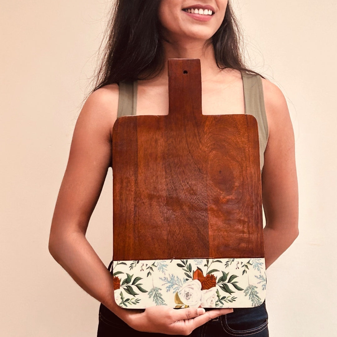 Model Holding a Mango Wood Cheese or Charcuterie Board  with print of white roses, pinecones and leaves on the bottom as a border