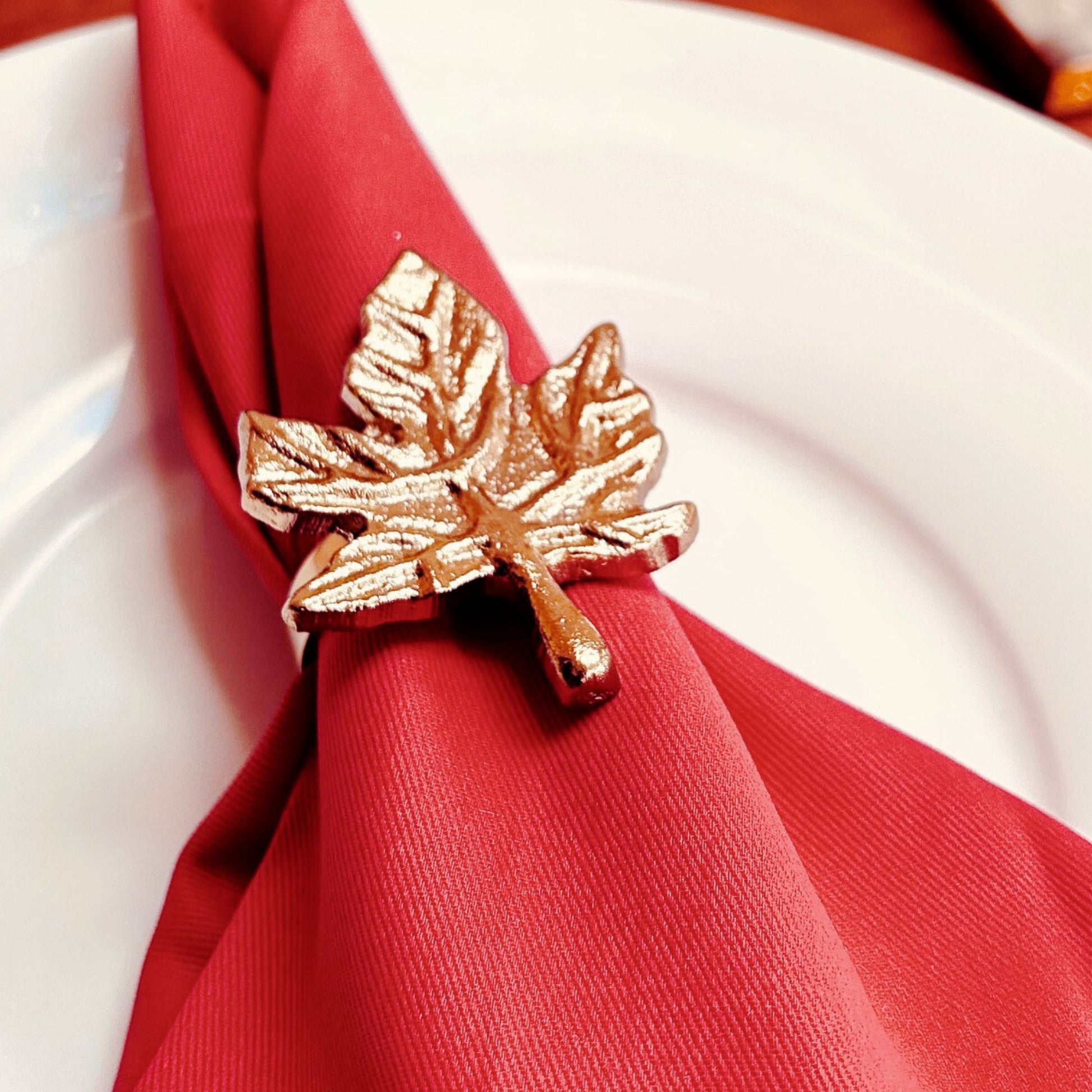 Gold finish Leaf design Napkin Ring placed on a red napkin ring kept on a white plate.