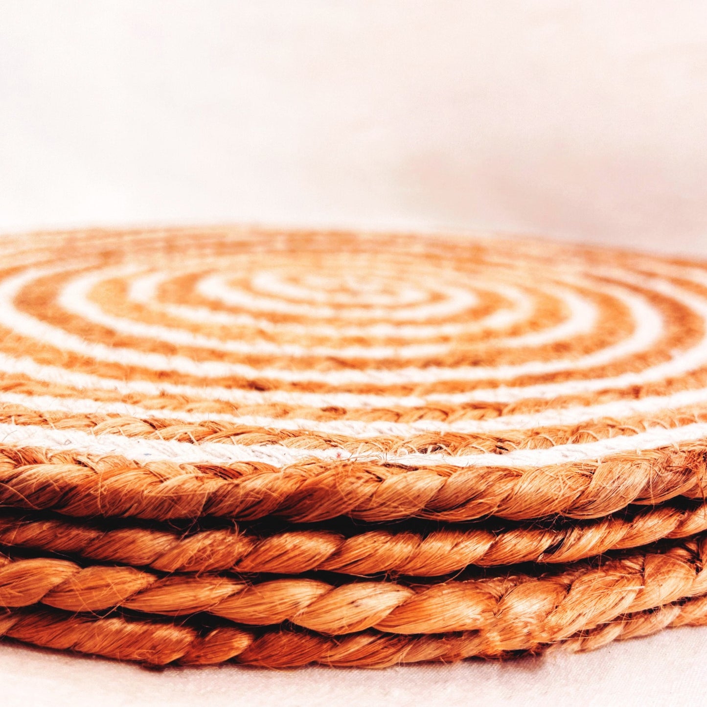 A stack of 4 100% Natural Round Jute and Cotton Braided Placemat in brown and white stripes.