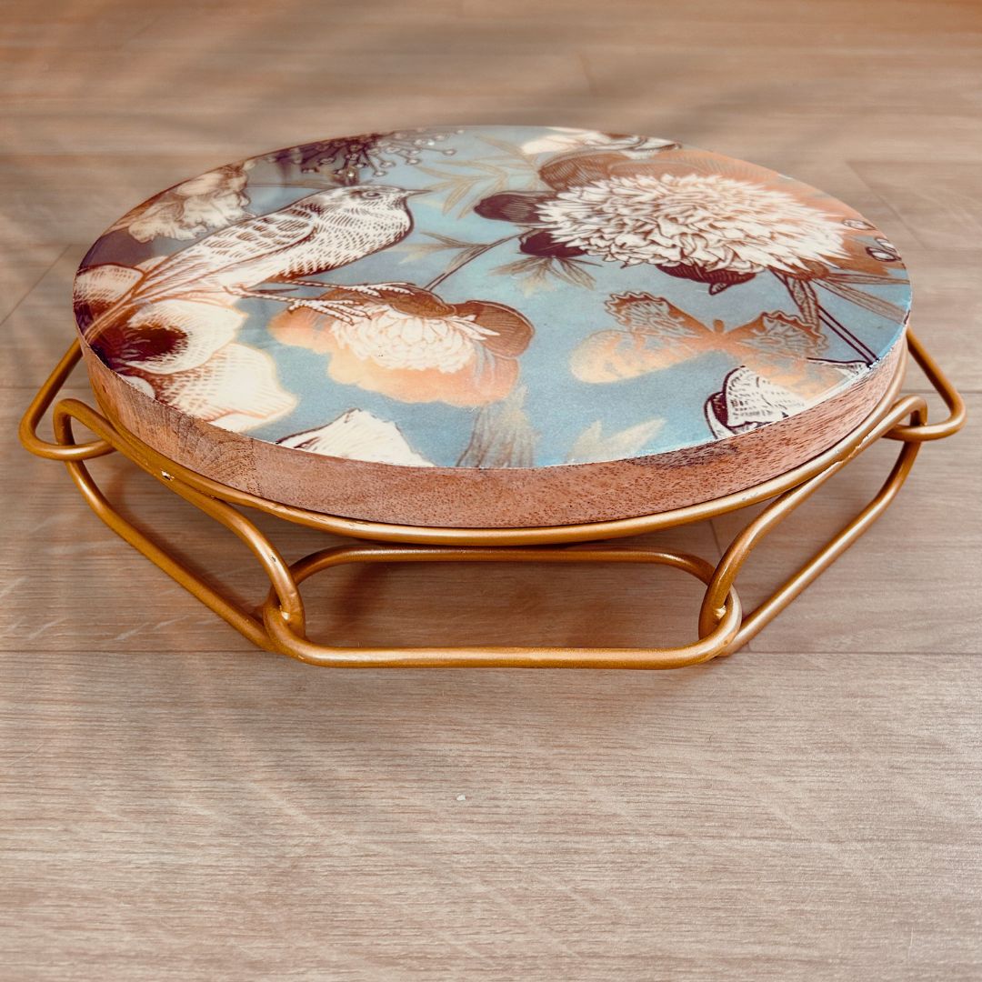 Cake Stand with Bird and flower print on a blue backdrop. The stand has an interlinked chain design in brushed gold.