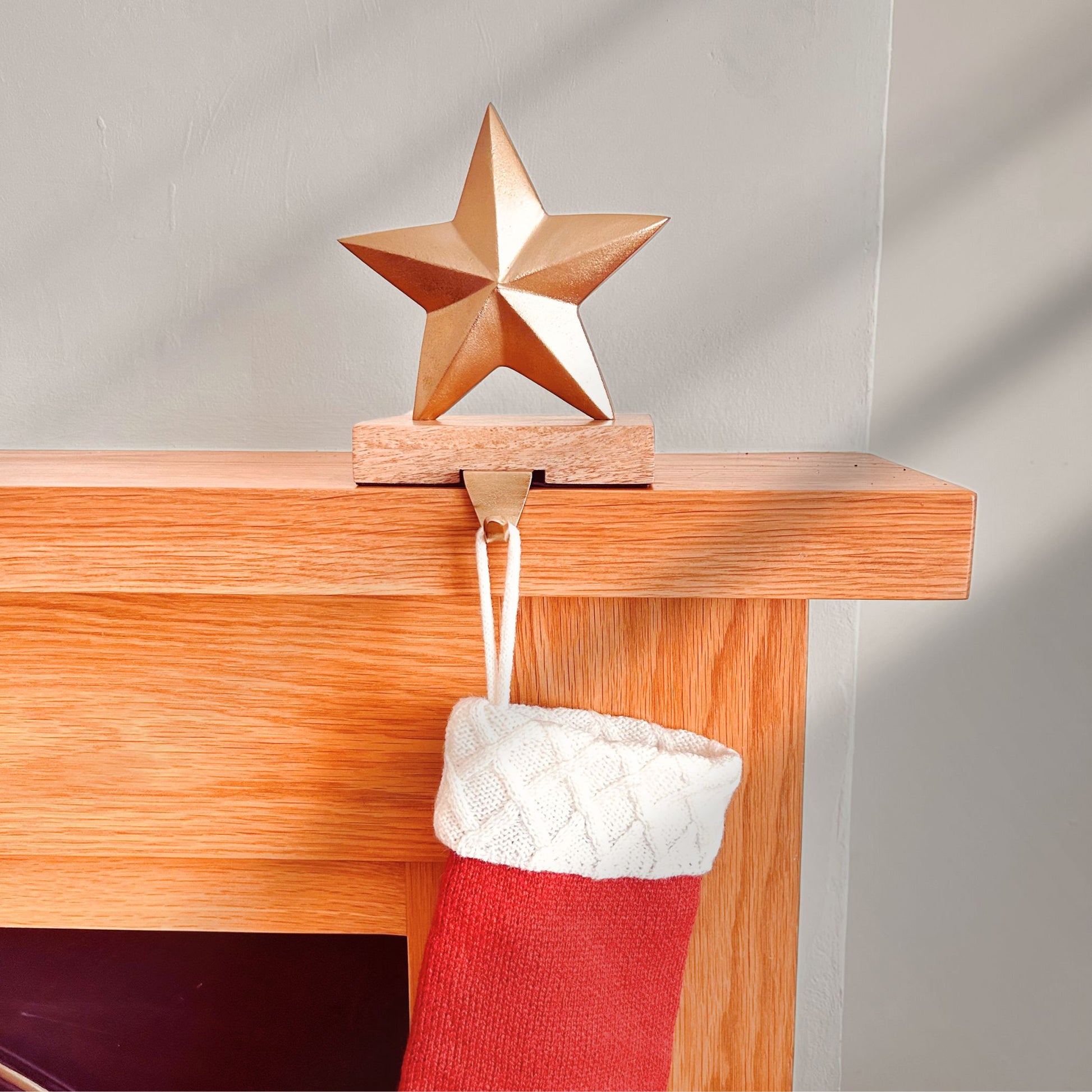 Brass Finish Star shaped stocking hanger on a wooden base kept on a mantle with a stocking hanging from it.