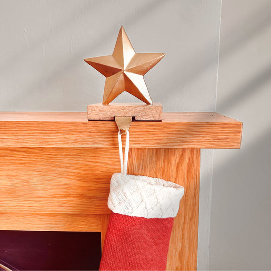 Brass Finish Star shaped stocking hanger on a wooden base kept on a mantle with a stocking hanging from it.