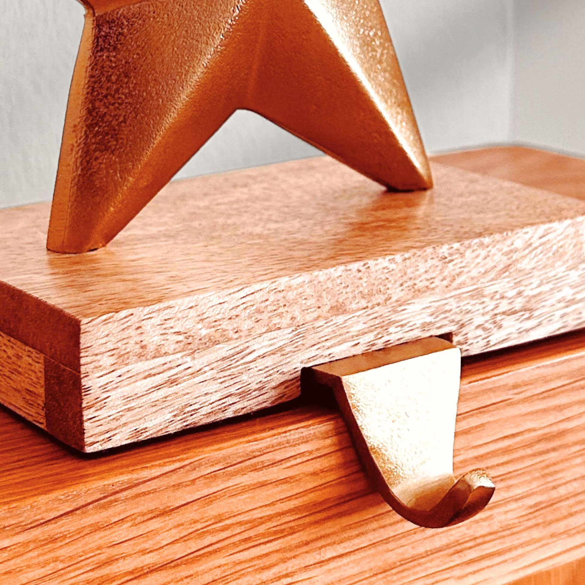 Close up shot of the hook of a Brass Finish Star shaped stocking holder on a wooden base kept on a mantle.