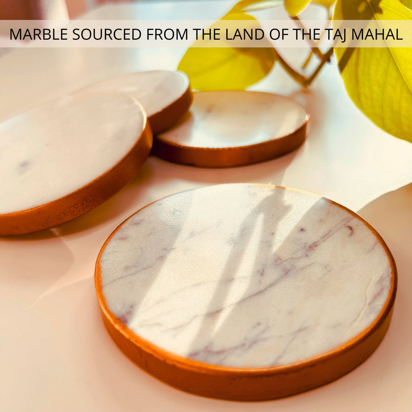 A set of 4 White round marble coasters with gold rim kept on a table.