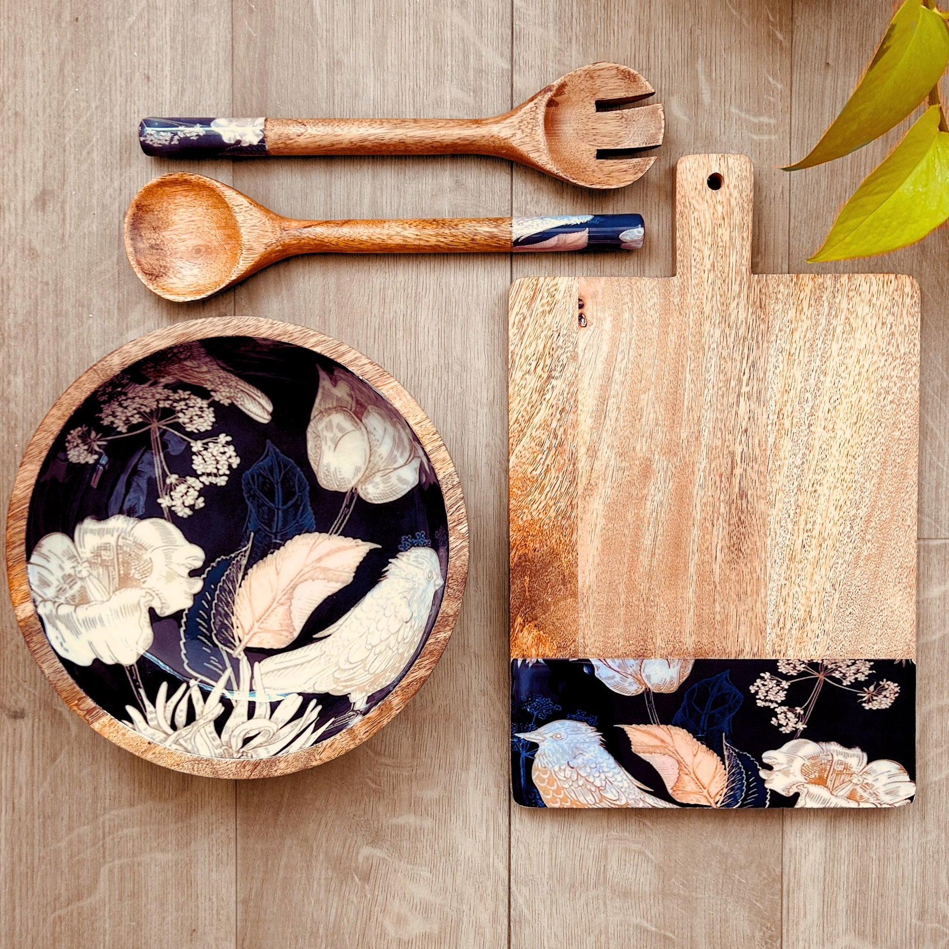 Gift set of a cheese board, salad bowl and salad servers with a print of bird, flowers and leaves on the bottom as a border