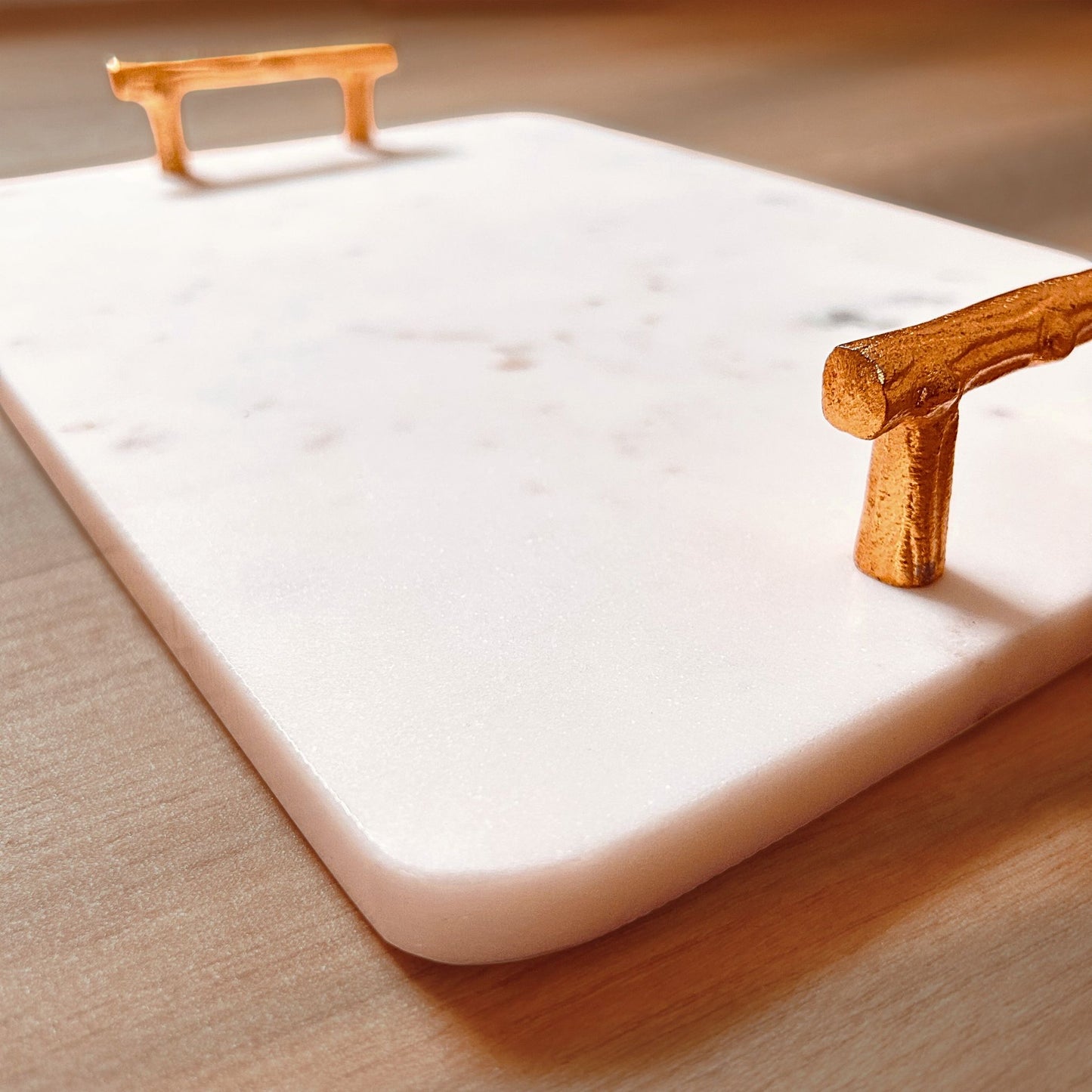 Close Up of a Rectangular White Marble Tray with Metal handles in gold finish kept on a wooden surface.