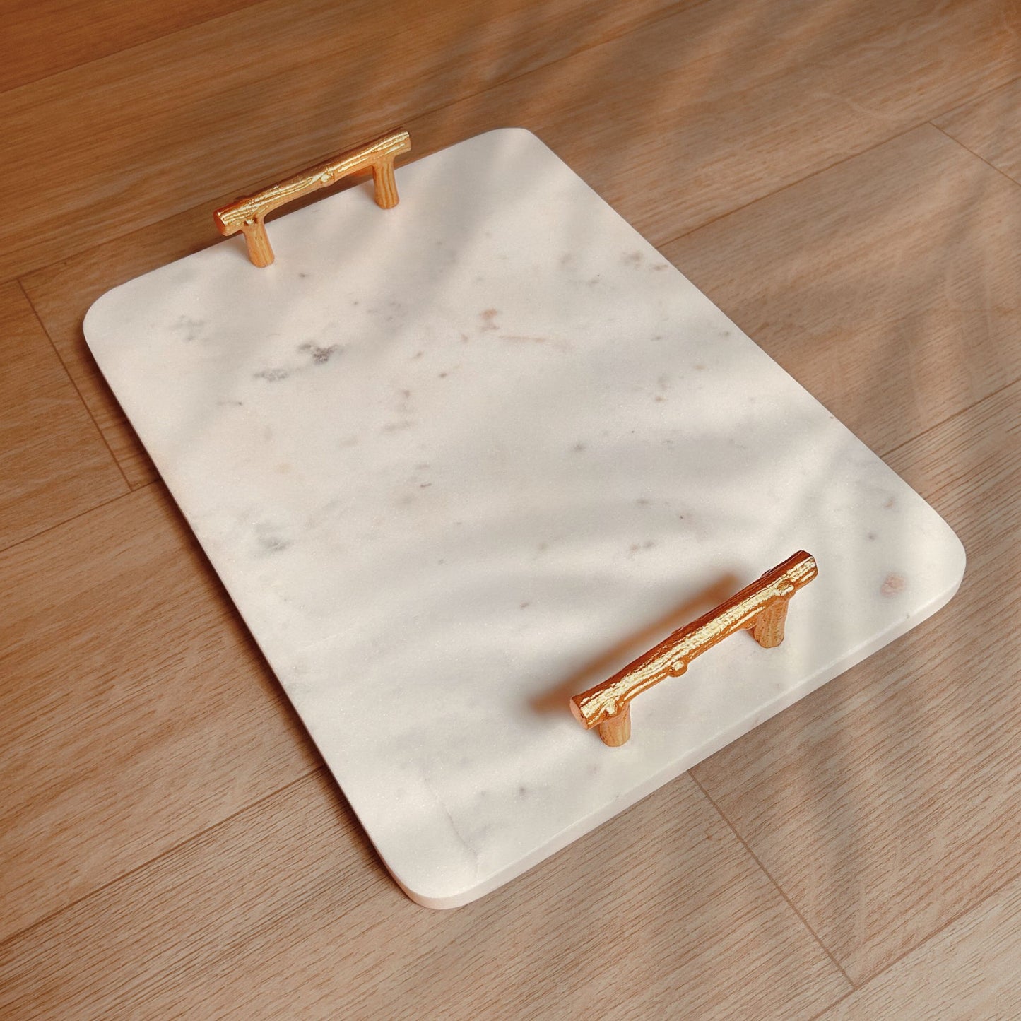 Rectangular White Marble Tray with Metal handles in gold finish kept on a wooden surface.