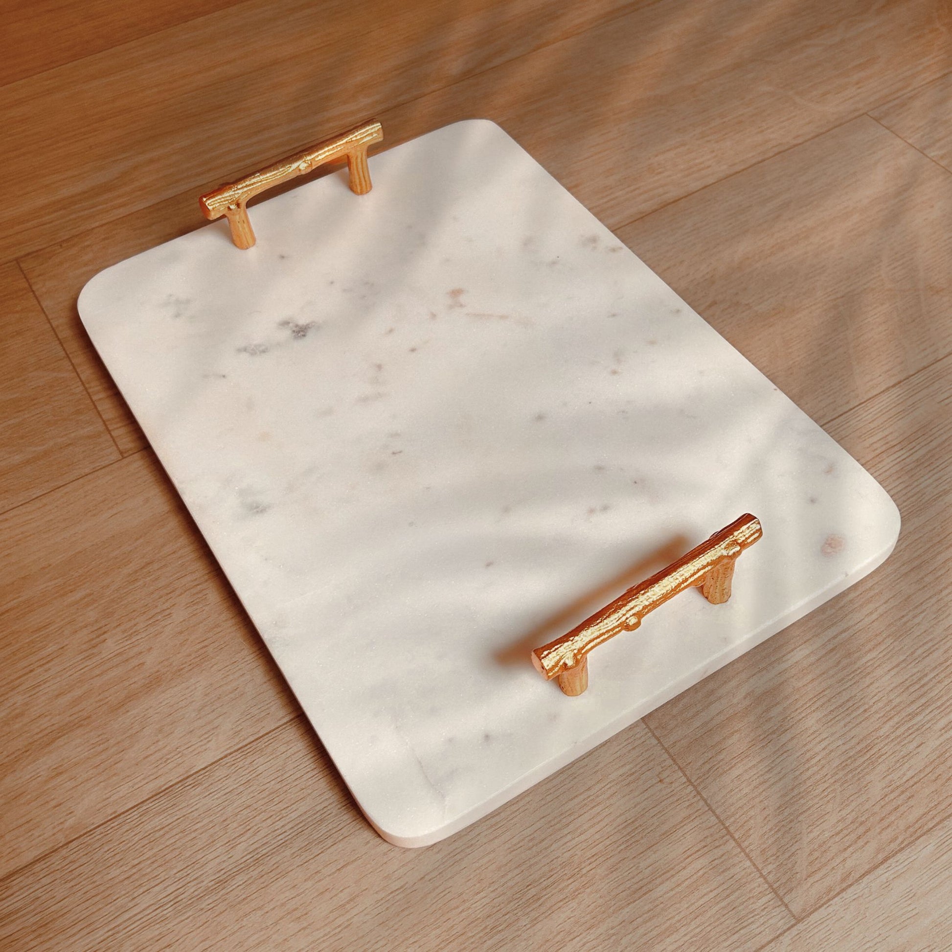 Rectangular White Marble Tray with Metal handles in gold finish kept on a wooden surface.