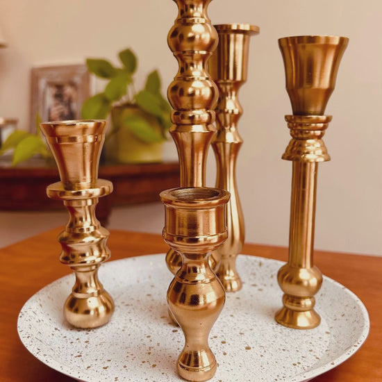 A product showcase of a 5 candle holder candelabra with a brass finish. The base is white with specks of gold on it.